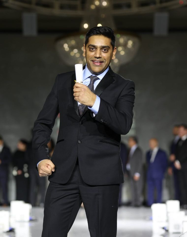 Robin Patel in a black suit holding an award at an awards evening.
