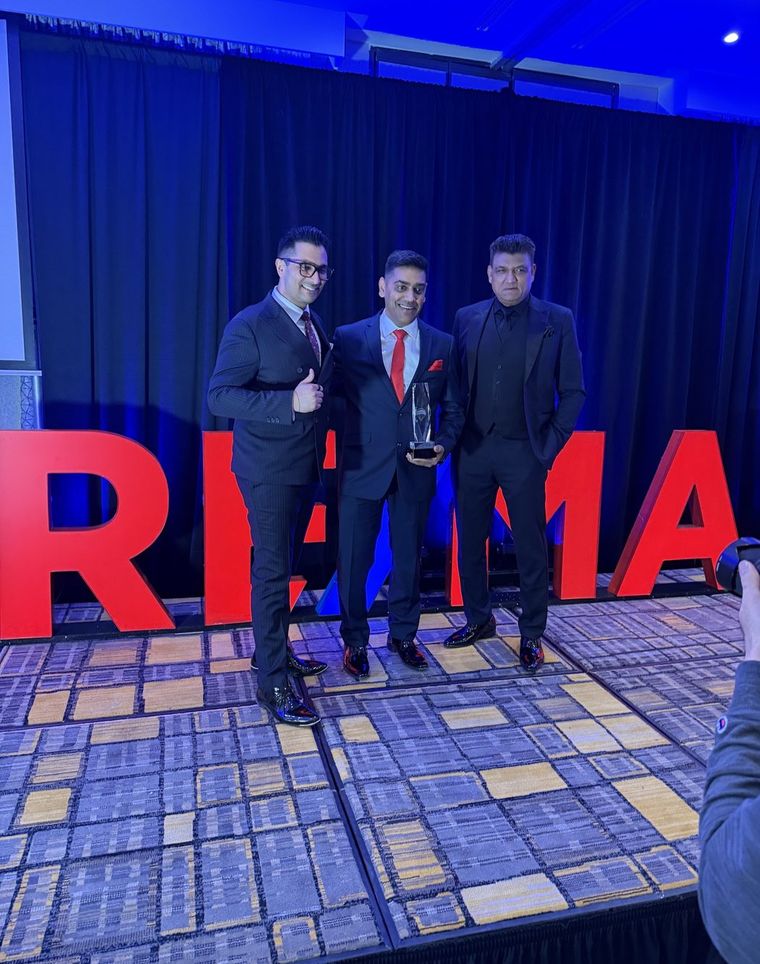 Robin Patel on stage with two colleagues in front of large illuminated RE/MAX lettering.