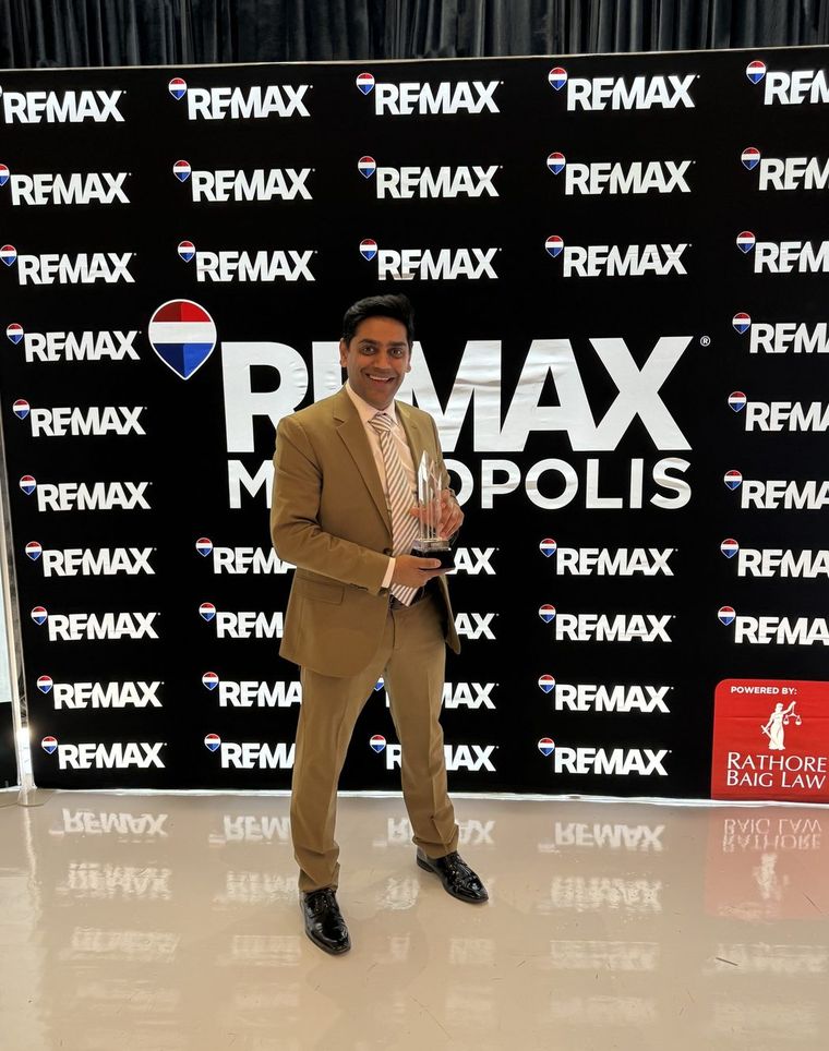 Robin Patel standing in front of a RE/MAX Metropolis Realty step-and-repeat backdrop.